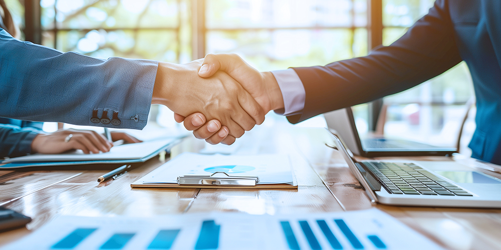 Los profesionales de negocios se dan la mano en una mesa de reuniones, rodeados de computadoras portátiles y documentos, simbolizando asociaciones exitosas en la industria de herramientas eléctricas.